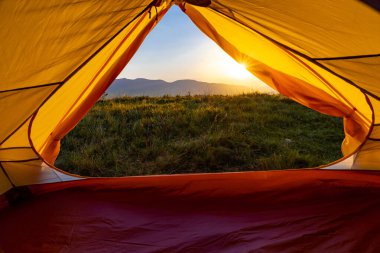 Dağın tepesinde gün batımı. Bir dağ manzarasının arka planında bir çadır.