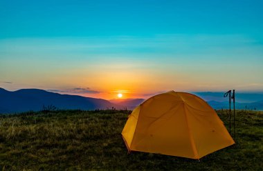 Dağın tepesinde gün batımı. Bir dağ manzarasının arka planında bir çadır.