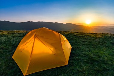 Dağın tepesinde gün batımı. Bir dağ manzarasının arka planında bir çadır.