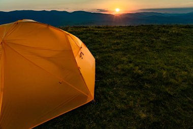 Dağın tepesinde gün batımı. Bir dağ manzarasının arka planında bir çadır.