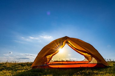 Dağın tepesinde gün batımı. Bir dağ manzarasının arka planında bir çadır.