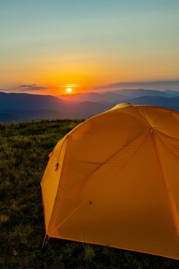 Dağın tepesinde gün batımı. Bir dağ manzarasının arka planında bir çadır.