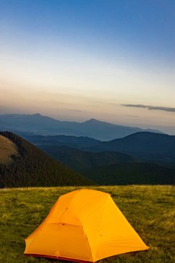 Dağın tepesinde gün batımı. Bir dağ manzarasının arka planında bir çadır.