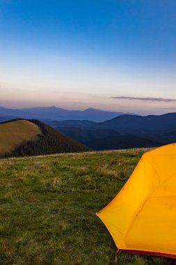 Dağın tepesinde gün batımı. Bir dağ manzarasının arka planında bir çadır.