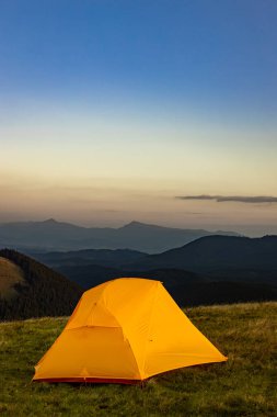 Dağın tepesinde gün batımı. Bir dağ manzarasının arka planında bir çadır.