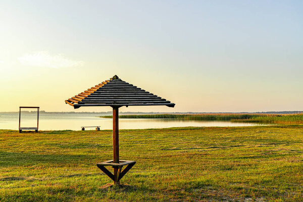 Один деревянный зонтик на пустом пляже возле озера.