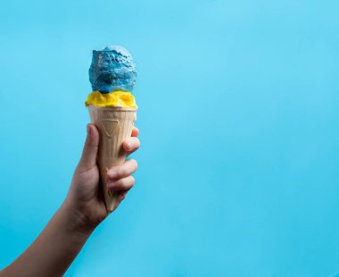 Gözleme kabında mavi-sarı dondurma Bir çocuk elinde bir külah tutuyor