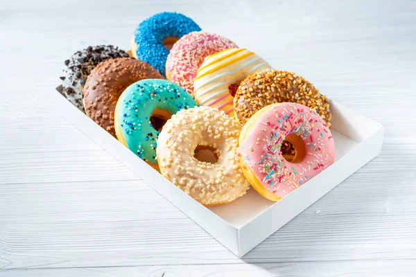 stock image Sweet donuts of different bright colors lie in a box on a white table