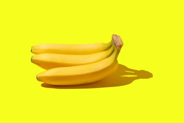 Sarı bir zemin üzerinde üç sarı olgun muz yatıyor.