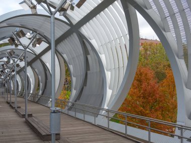 Etrafı turuncu ağaçlarla çevrili metal boru şeklinde bir köprü.