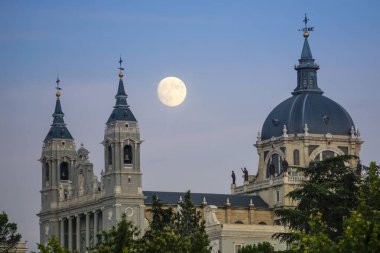 Sunset image of the Almudena Cathedral in Madrid with the full moon in the background clipart
