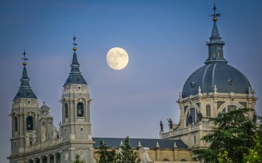 Sunset image of the Almudena Cathedral in Madrid with the full moon in the background clipart