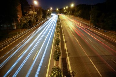 Sokak lambalarıyla aydınlatılmış bir otoyolda araç ışıkları görülüyor.