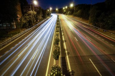 Sokak lambalarıyla aydınlatılmış bir otoyolda araç ışıkları görülüyor.