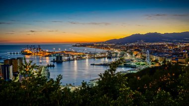 Gün batımında Malaga şehrinin panoramik manzarası. Önde liman, arkada dağlar.