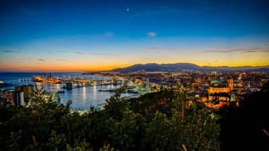 Gün batımında Malaga şehrinin panoramik manzarası. Önde liman, arkada dağlar.