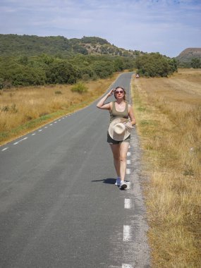 Arka planda ezilmiş saman balyalarıyla yolda yürüyen bir kadın.