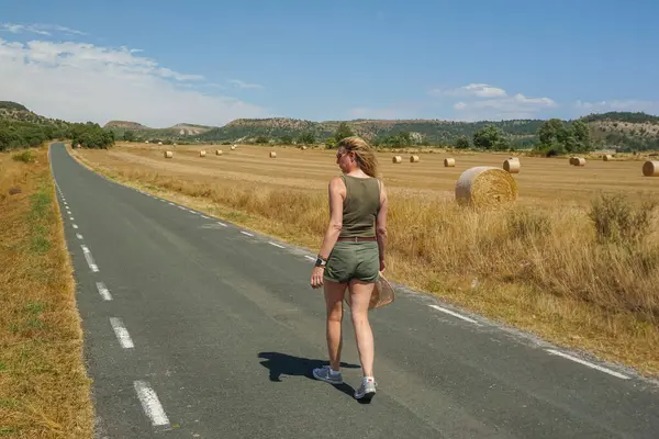Arka planda ezilmiş saman balyalarıyla yolda yürüyen bir kadın.