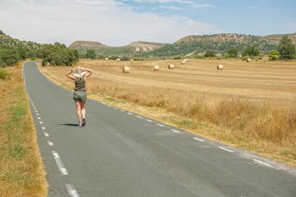 Arka planda ezilmiş saman balyalarıyla yolda yürüyen bir kadın.
