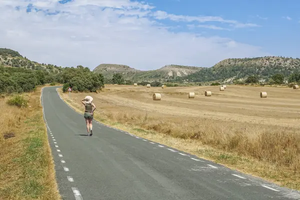 Arka planda ezilmiş saman balyalarıyla yolda yürüyen bir kadın.