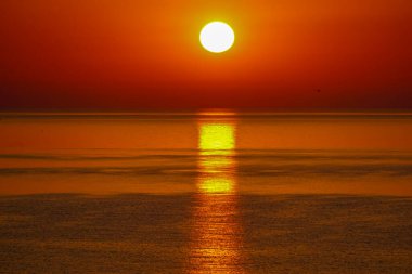 Güneş, alacakaranlıkta kırmızımsı tonlarla denizin üzerinde batıyor.