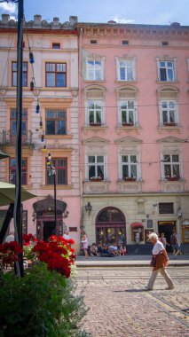 Yaşlı kadın eski pembe binanın önünden geçiyor. Ana meydan, Lviv, Ukrayna. Yaz günü.