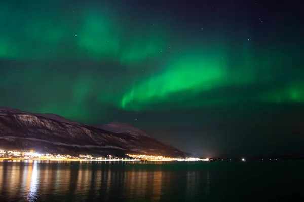 Yeşil aurora borealis, kuzey ışığı. Tromso, Norveç. Norveç 'te kış. Çatı pencereleri. Uzun pozlama. Nefes kesici. Kozmik enerji. İyi geceler gökyüzü. Tromso 'yu ziyaret et. Kuzey görüşü. Gece kasabası suya yansıyor. 