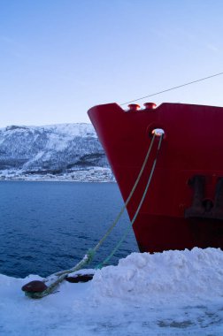 Limandaki kırmızı geminin burnu, Tromso, Norveç 'te. Kışın kar, fiyort, soğuk. Kutup dairesi, su üzerinde, akşam. 
