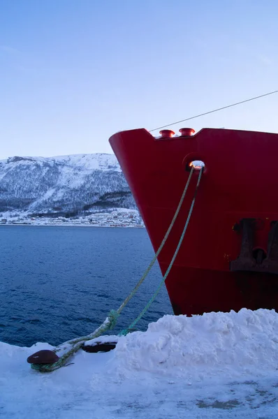 Limandaki kırmızı geminin burnu, Tromso, Norveç 'te. Kışın kar, fiyort, soğuk. Kutup dairesi, su üzerinde, akşam. 
