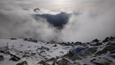 Bulutlar arasındaki dinginlik: karlı bir dağın zirvesinden bulutların arasından geçen nefes kesici bir manzara.
