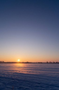 Erken kış şafağı bozulmamış kar üzerinde; sakin sabah güneşi donmuş manzaranın üzerinde yükselir; altın güneş ışığı sakin kış sükunetini kapsar.