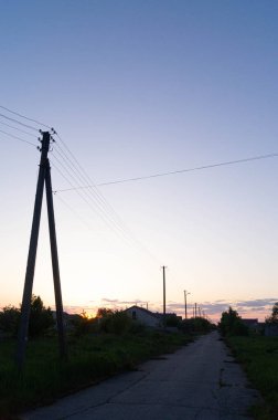 Elektrik direkleriyle dolu bir kır yolu üzerinde dramatik bir gün batımı, elektrik hattı siluetleri olan kırsal bir cadde boyunca sakin bir alacakaranlık, canlı bir günbatımı arka planına karşı sakin ve ıssız bir yol..
