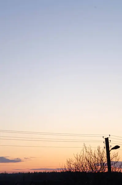 Urban sunset skyline silhouetted against a gradient sky; minimalist dusk landscape in a suburban setting, showcasing tranquil twilight with streetlamp and powerlines.