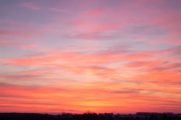 A vibrant sunrise splashes the sky with warm colors, signaling a new day. Horizon alive with fiery hues as morning breaks, promising a fresh start. Strokes of pink and orange awaken the world.