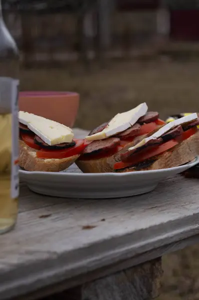 Rustic sandwich on a plate with refreshing cider, outdoor dining. Alfresco meal with a hearty sandwich and a side of cold beer. Casual outdoor feast, a sandwich paired with chilled cider. Picnic setting with a gourmet sandwich and a bottle of cider.