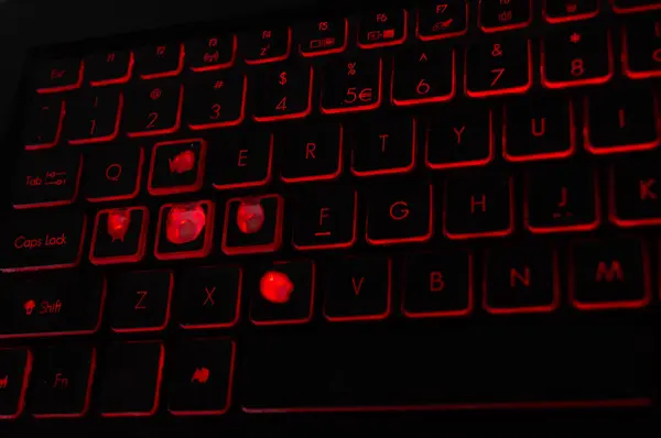 Illuminated gaming keyboard with worn keys, ideal for tech blogs and gaming setups. Backlit mechanical keyboard with signs of heavy use, perfect for articles on gaming gear durability. Red LED keyboard highlighting the reality of avid gaming.