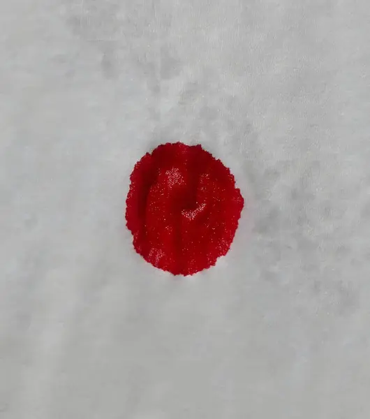 A single drop of red blood stands out against a crisp white napkin. Stark contrast of a vibrant blood drop on a pure white background. The vivid red of a fresh blood droplet creates a striking image on white.