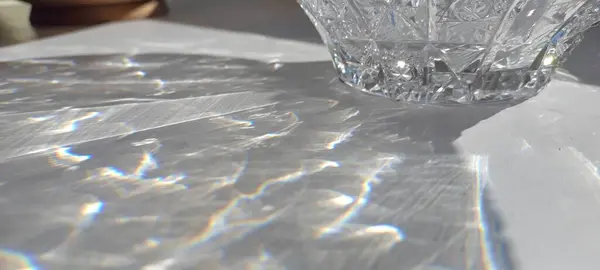 stock image Sunlit crystal bowl casting a dazzling spectrum of light on a smooth table surface, capturing the intricate beauty of refracted sunlight in an everyday setting.