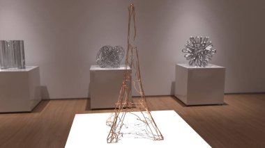 Modern art gallery showcasing wire sculptures on white pedestals in a minimalist setting with soft lighting. clipart