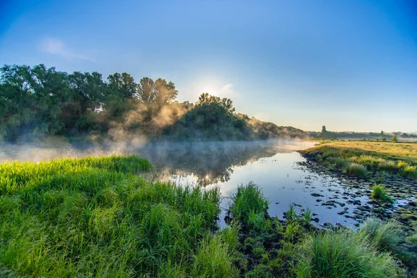 stock image Landscape with sunrise. The sun comes out from behind the forest over the river with fog