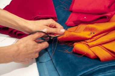 Hands with black scissors, pieces of velvet fabric. Velvet fabric blue, red and orange colours