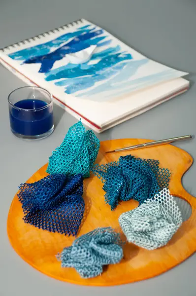 Fabric mesh samples in blue on wood palette, pattern with waves and paper boat