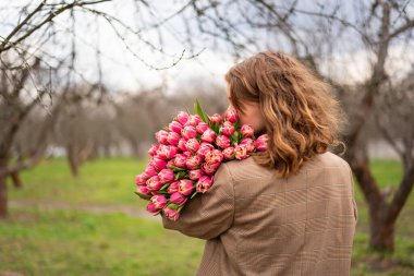 Büyük bir buket pembe laleli, bej ceketli sarışın kız.