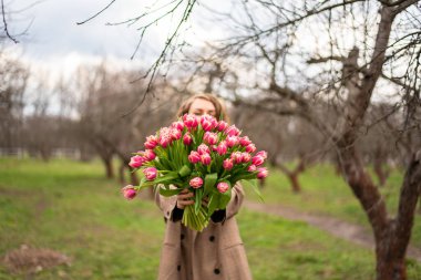 Ağaç zemininde bir kızın ellerinde büyük bir buket pembe lale.