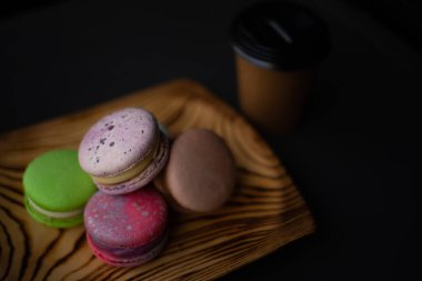 Ahşap bir tabakta pembe ve açık yeşil makarna kekleri ve bir kağıt bardak.