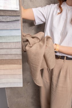 Tasarımcı kumaşları seçer. Beyaz tişörtlü ve bej pantolonlu bir kızın ellerinde kumaş örnekleri..