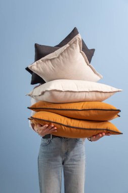 The girl holds a stack of decorative colored pillows on a blue background. Decorative cushions for the sofa and bed. clipart