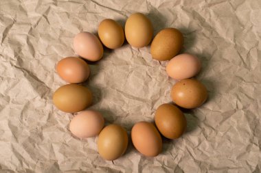 Kırışmış kağıtta Paskalya desenli kahverengi yumurta çelengi. Kırışmış kahverengi kağıdın arka planında yumuşak ışıkta kahverengi tavuk yumurtası..