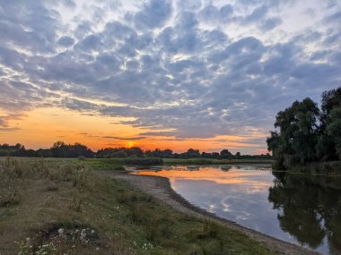 Parlak günbatımı. Gökyüzünün arkasında bulutlu ve günbatımlı bir nehir manzarası.