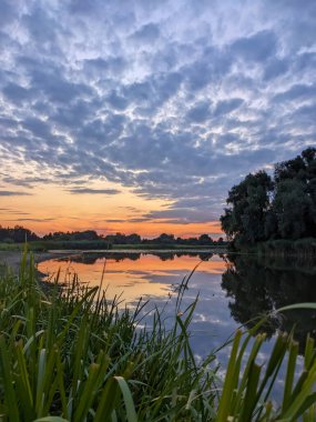 Parlak günbatımı. Gökyüzünün arkasında bulutlu ve günbatımlı bir nehir manzarası.